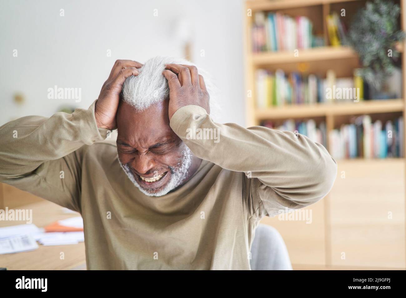 Senior man suffering from headache while sitting in living room Stock Photo