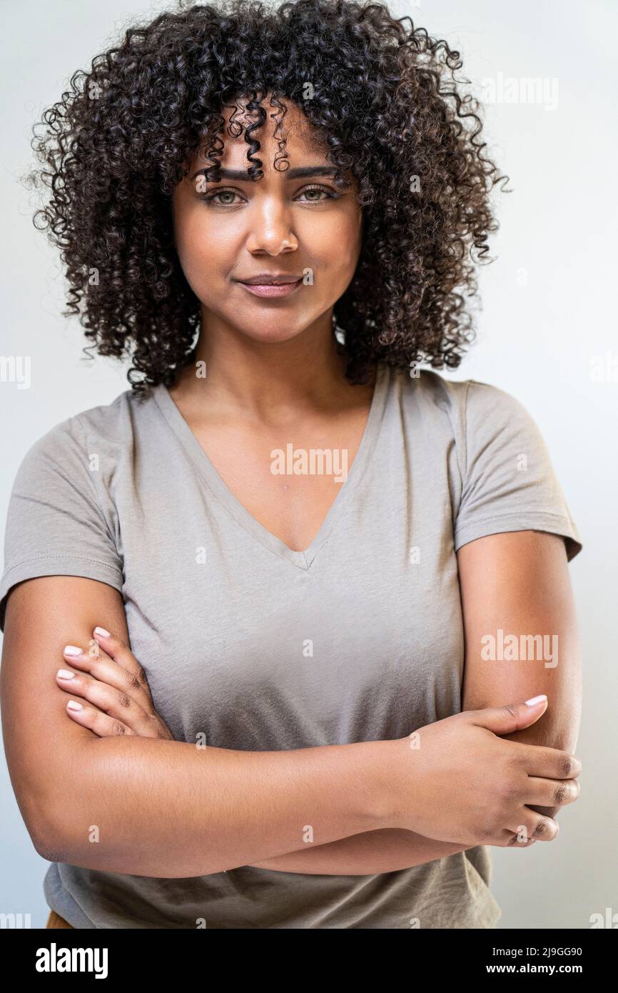Woman with arms crossed standing against white wall Stock Photo