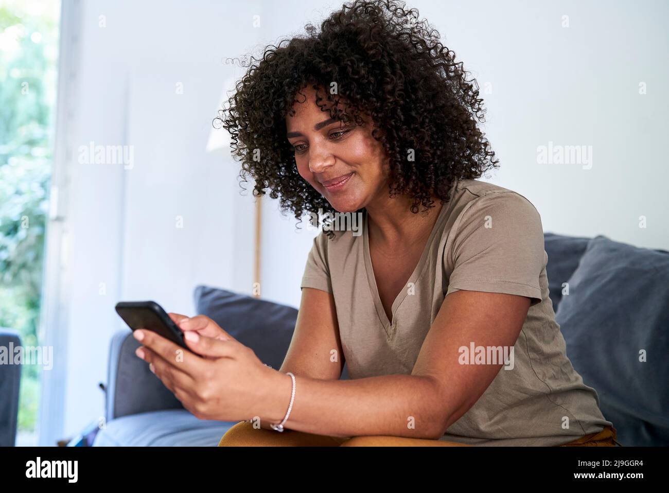 Woman using smart phone while sitting in living room Stock Photo