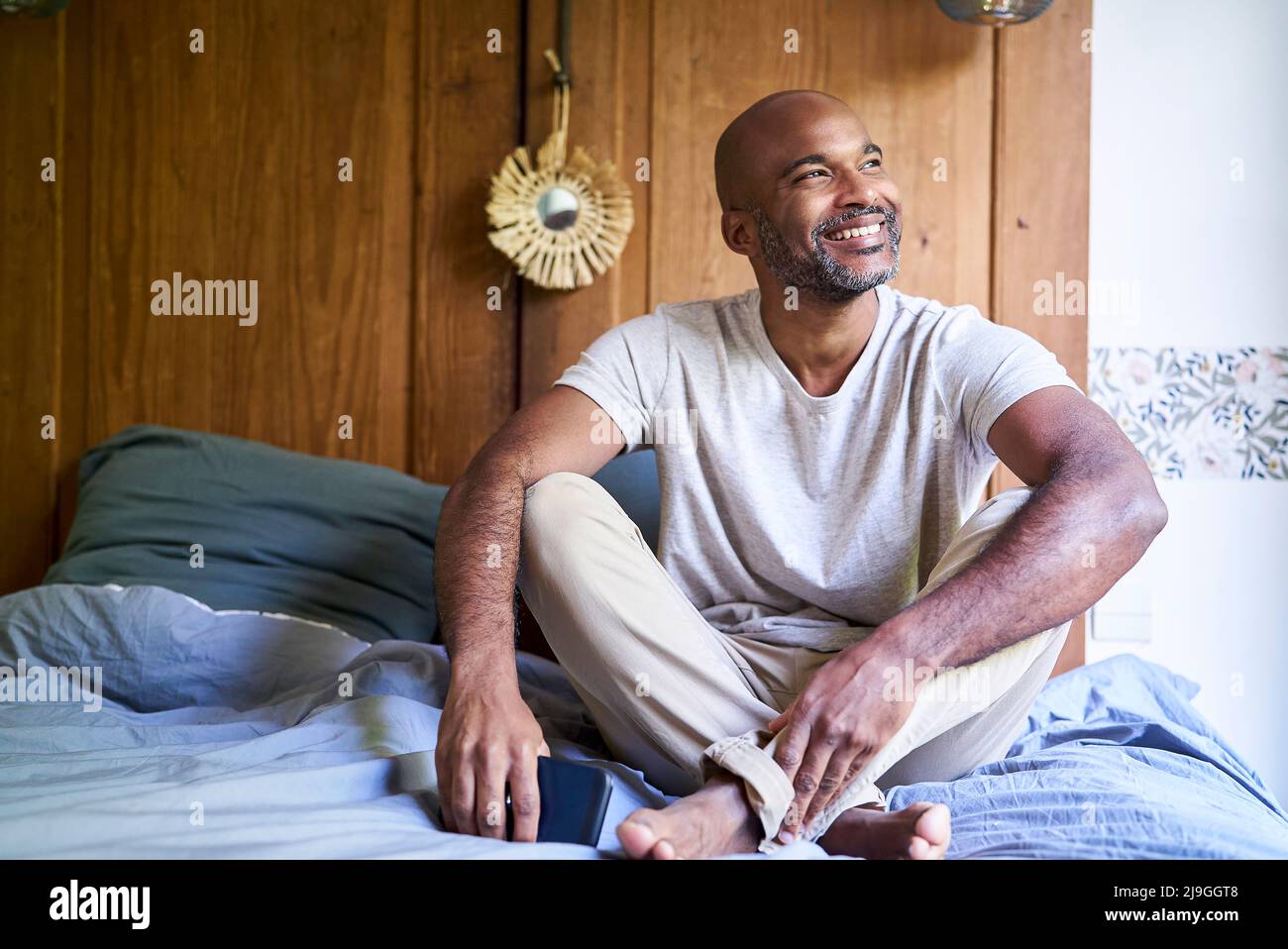 Smiling man holding smart phone while sitting in bedroom Stock Photo