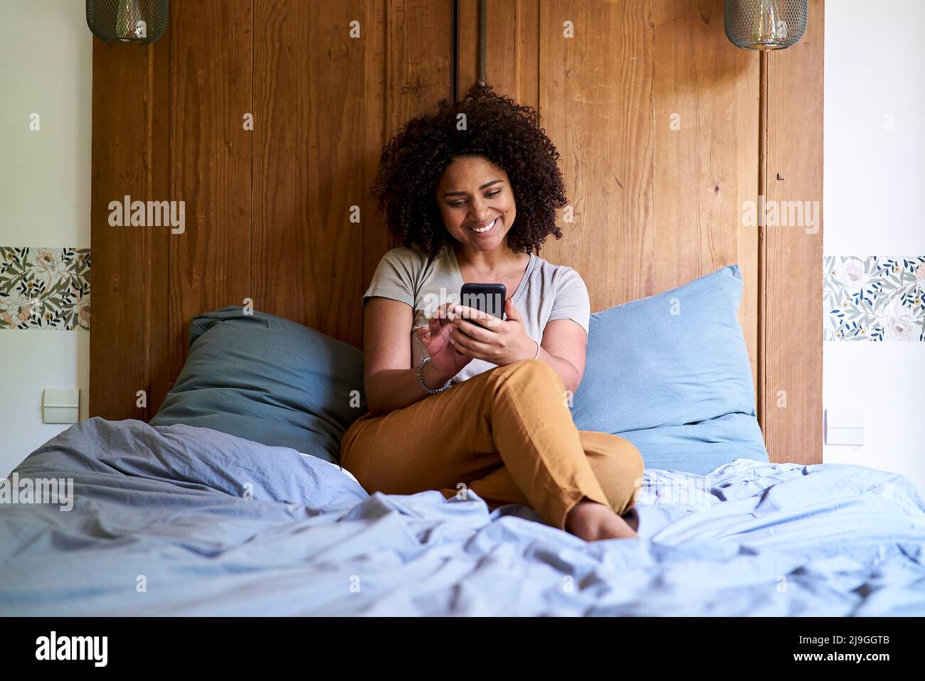 Woman using smart phone while sitting in bedroom Stock Photo