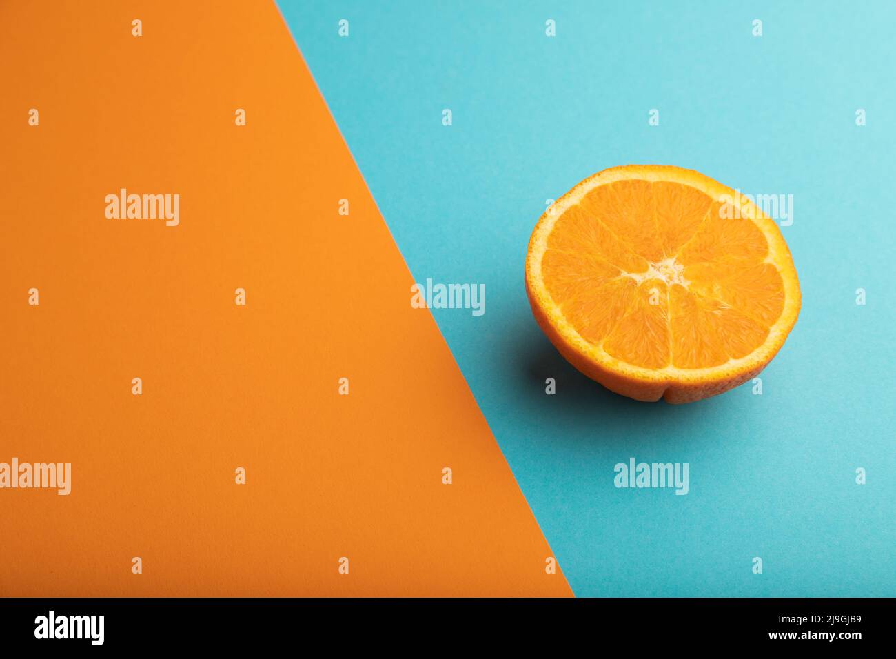 Ripe cut orange on orange and blue pastel background. Side view, copy space. Tropical, healthy food, concept, minimalism. Stock Photo