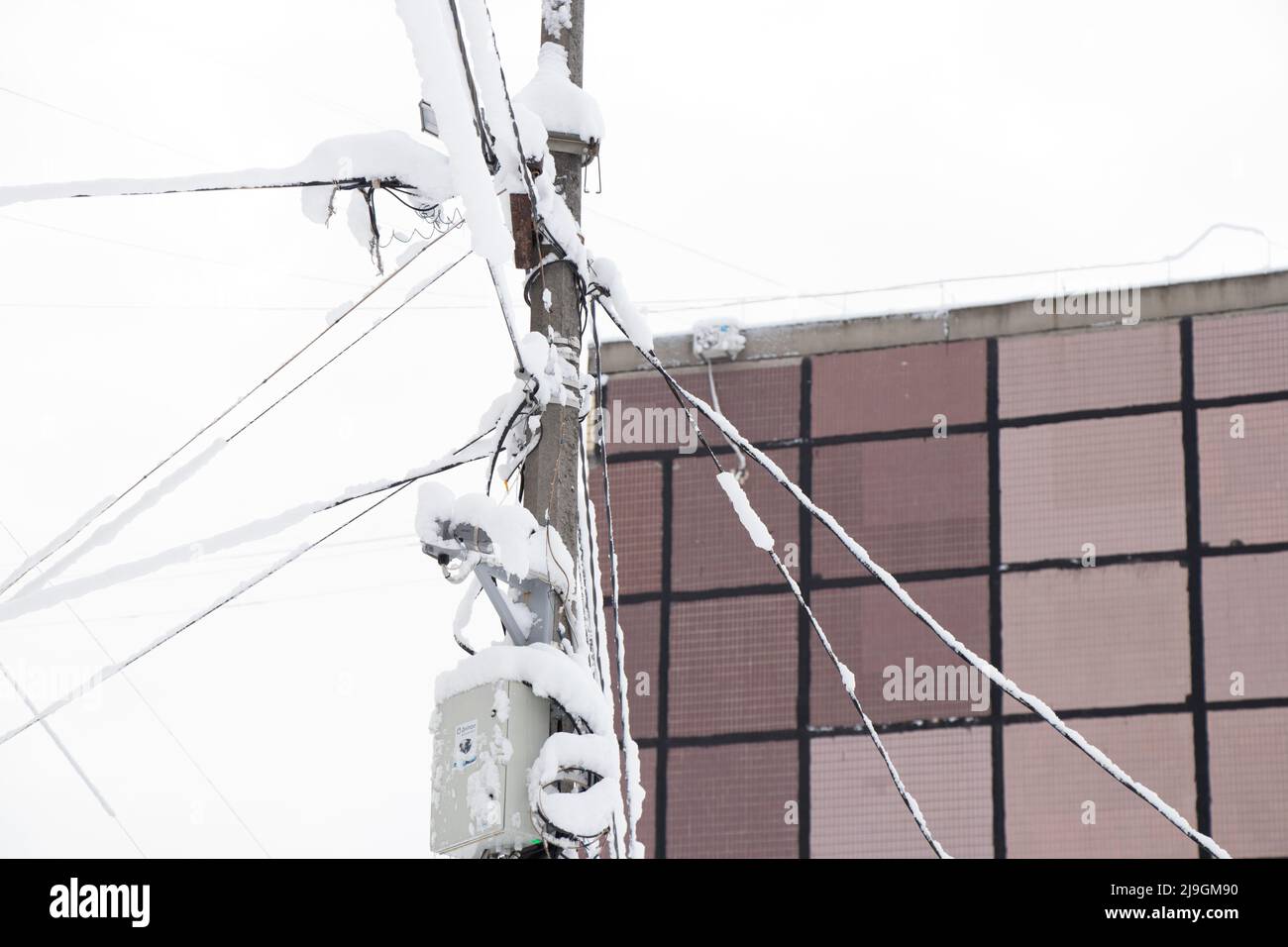 Electric wires in the snow with ice on a pole in a residential area of the city, sagging wires from the severity of snow in the city of Dnipro in Ukra Stock Photo