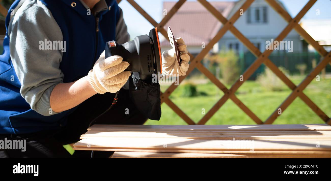 female hands in gloves are engaged in grinding the surface of a wooden table. Construction concept Stock Photo