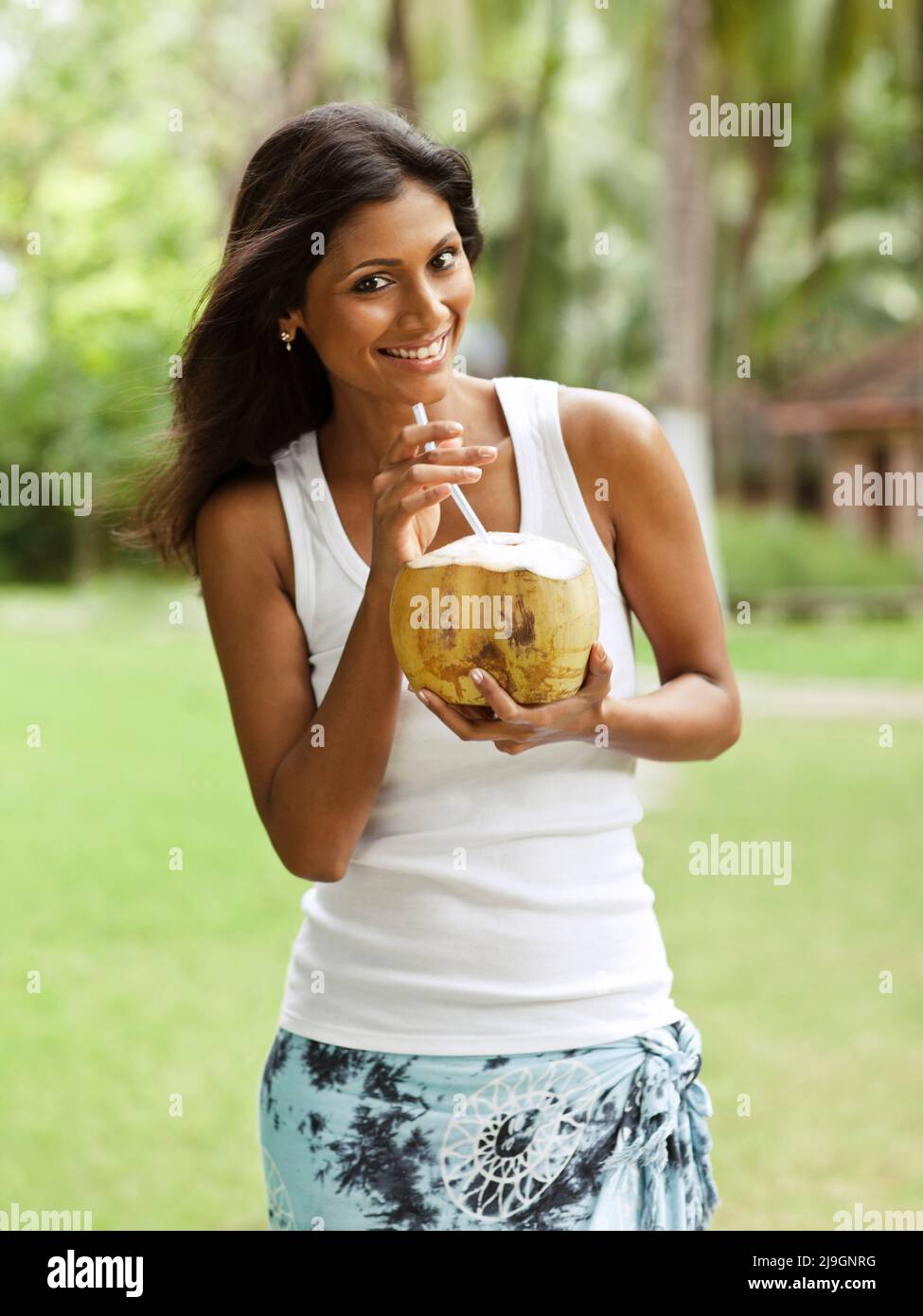 A woman drinks a freshly cut coconut on the lawn at Kairali Ayurvedic Health Resort. Kairali Ayurvedic Health Resort, Palakkad, Kerala, India. Stock Photo