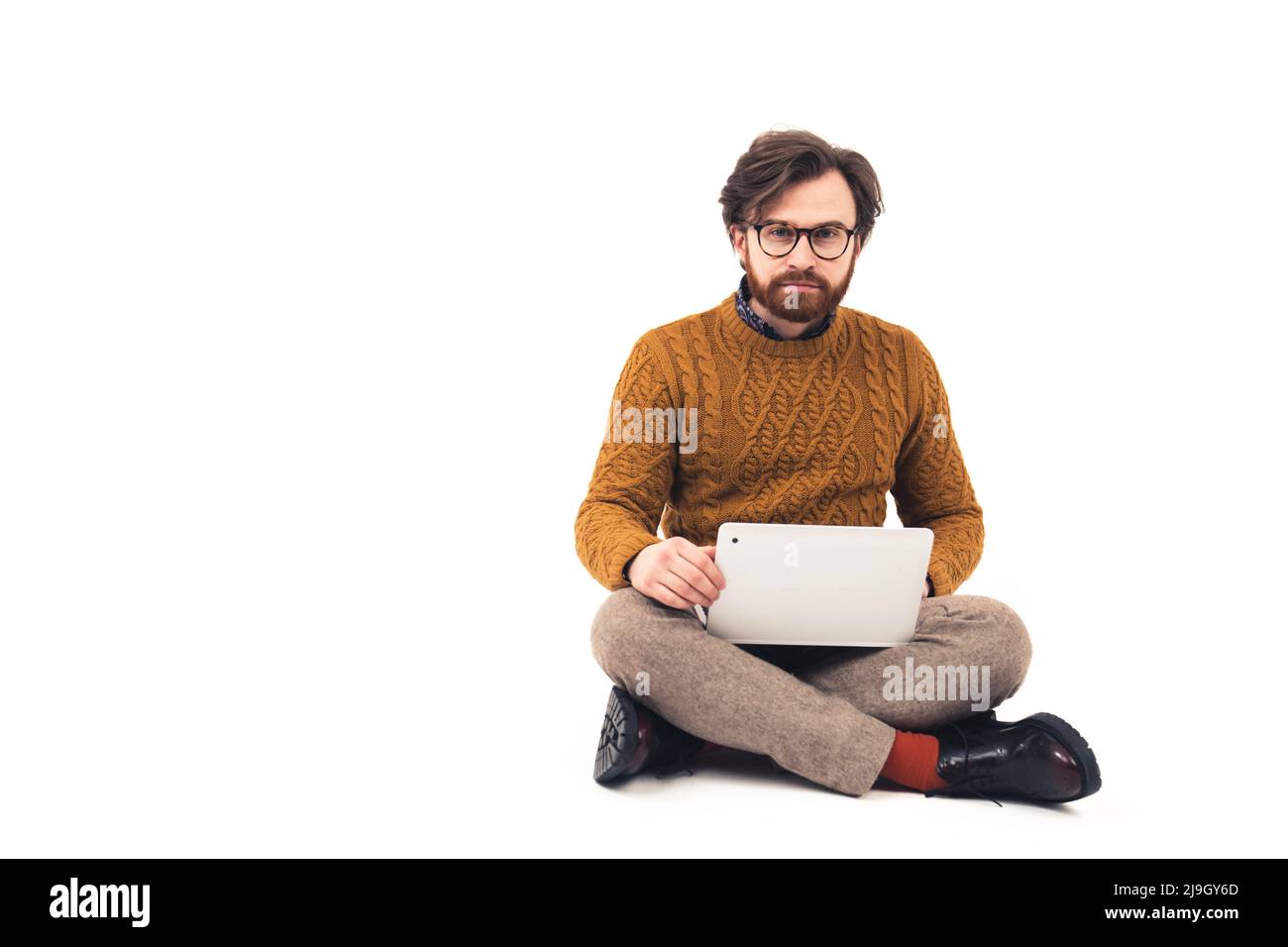 Intrigued caucasian social media male user sits on the floor in studio with laptop on knees over white background. High quality photo Stock Photo