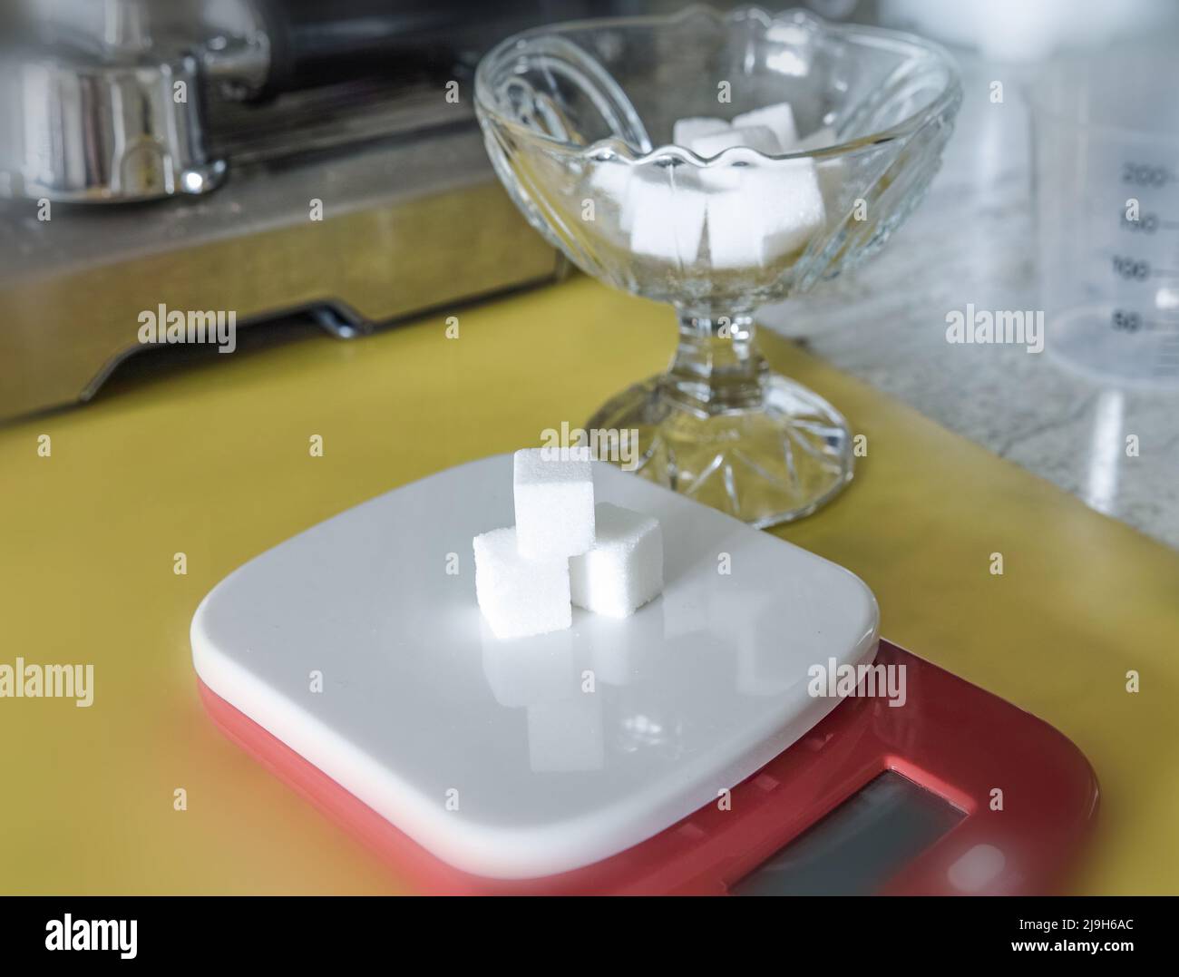 Sugar cubes on an electronic scale, in the kitchen. A crystal cup as well Stock Photo Alamy