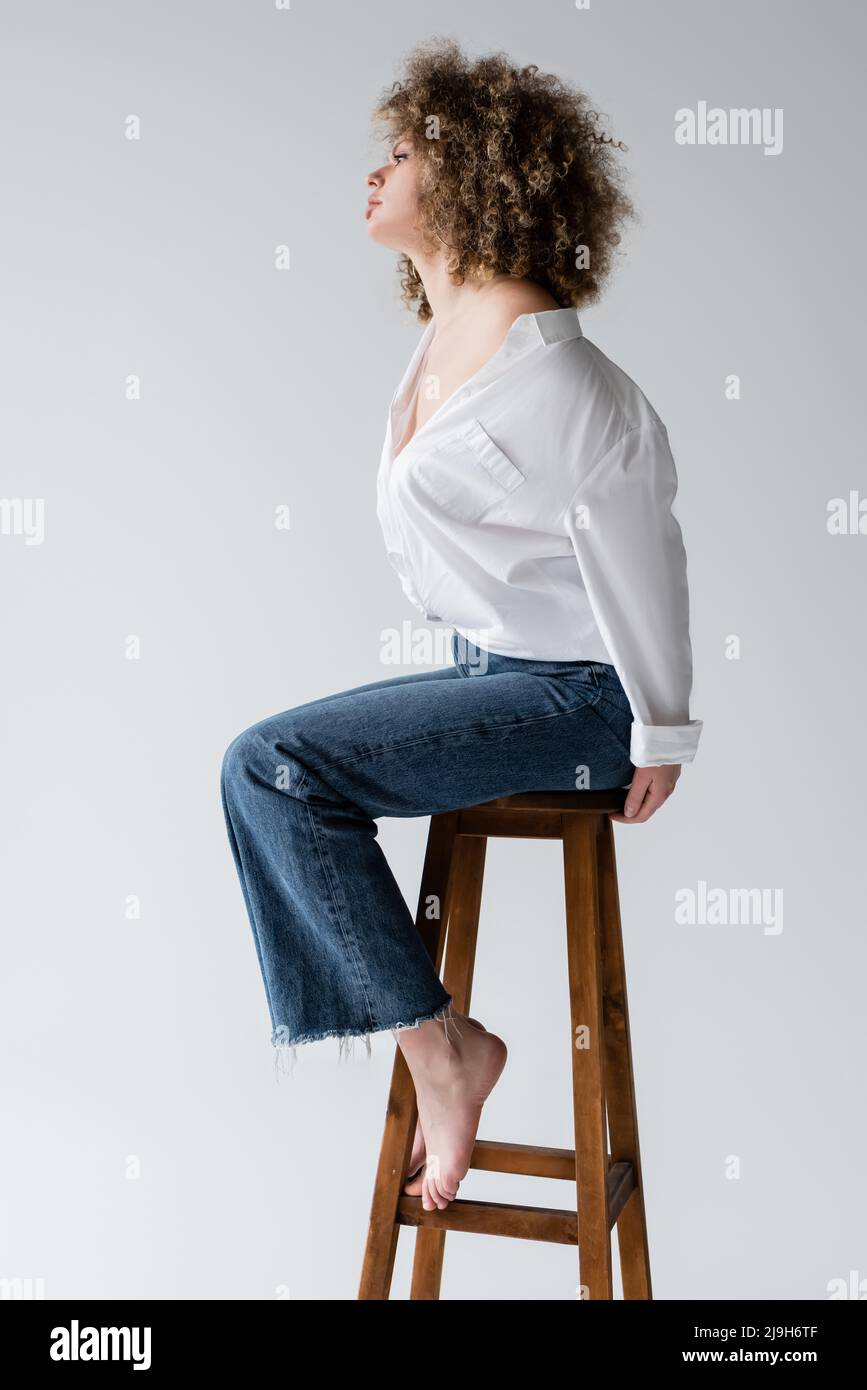 Side view of stylish barefoot model sitting on chair isolated on white Stock Photo