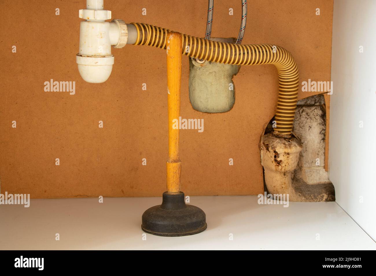 A plunger stands in a cupboard under the sink in the kitchen, cleaning clogged pipes, an old pipe cleaner Stock Photo