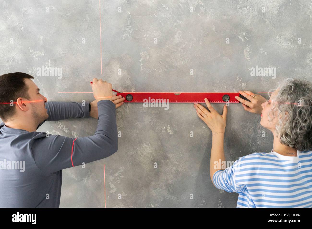 Woman with friend measuring gray wall with level Stock Photo - Alamy