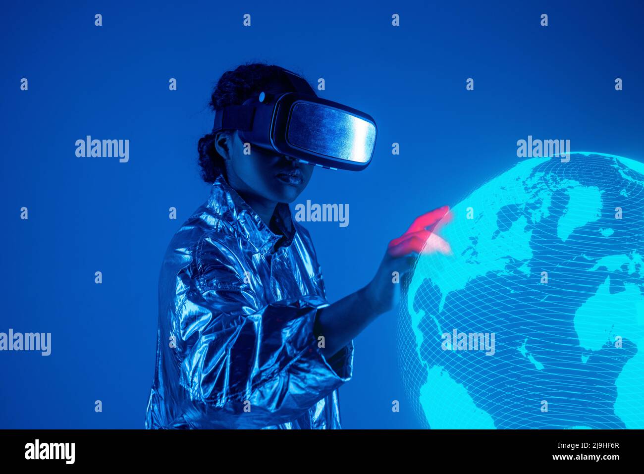 Woman wearing virtual reality simulator touching earth on screen against blue background Stock Photo