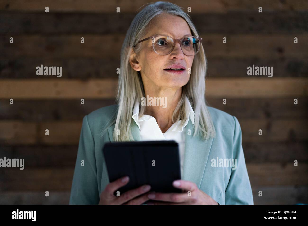 Contemplative businesswoman holding tablet PC in front of wall Stock Photo