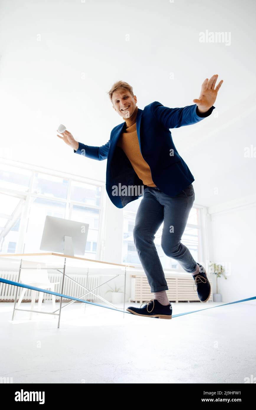 Happy businessman balancing on tightrope in office Stock Photo