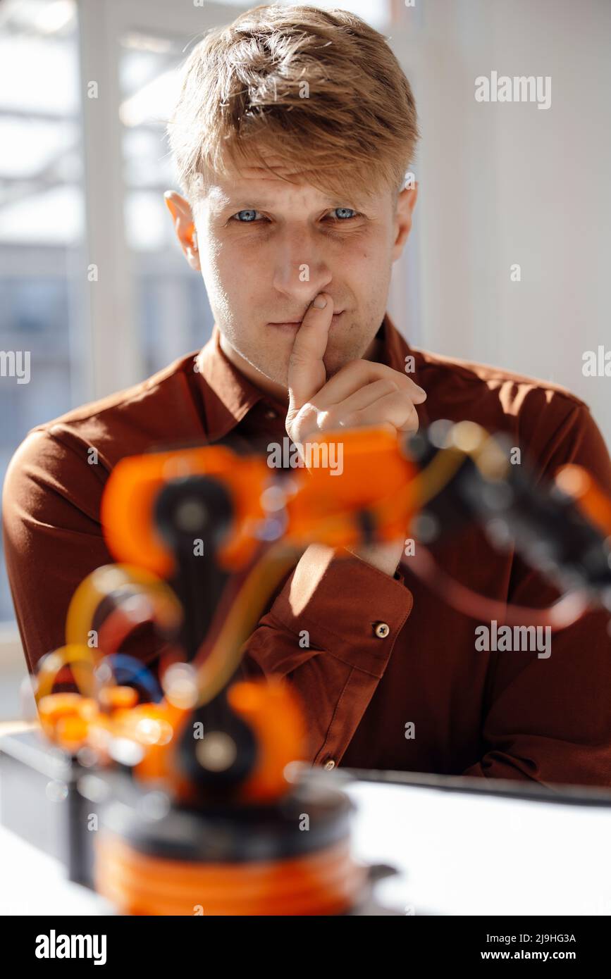 Thoughtful businessman looking at model of robotic arm in office Stock