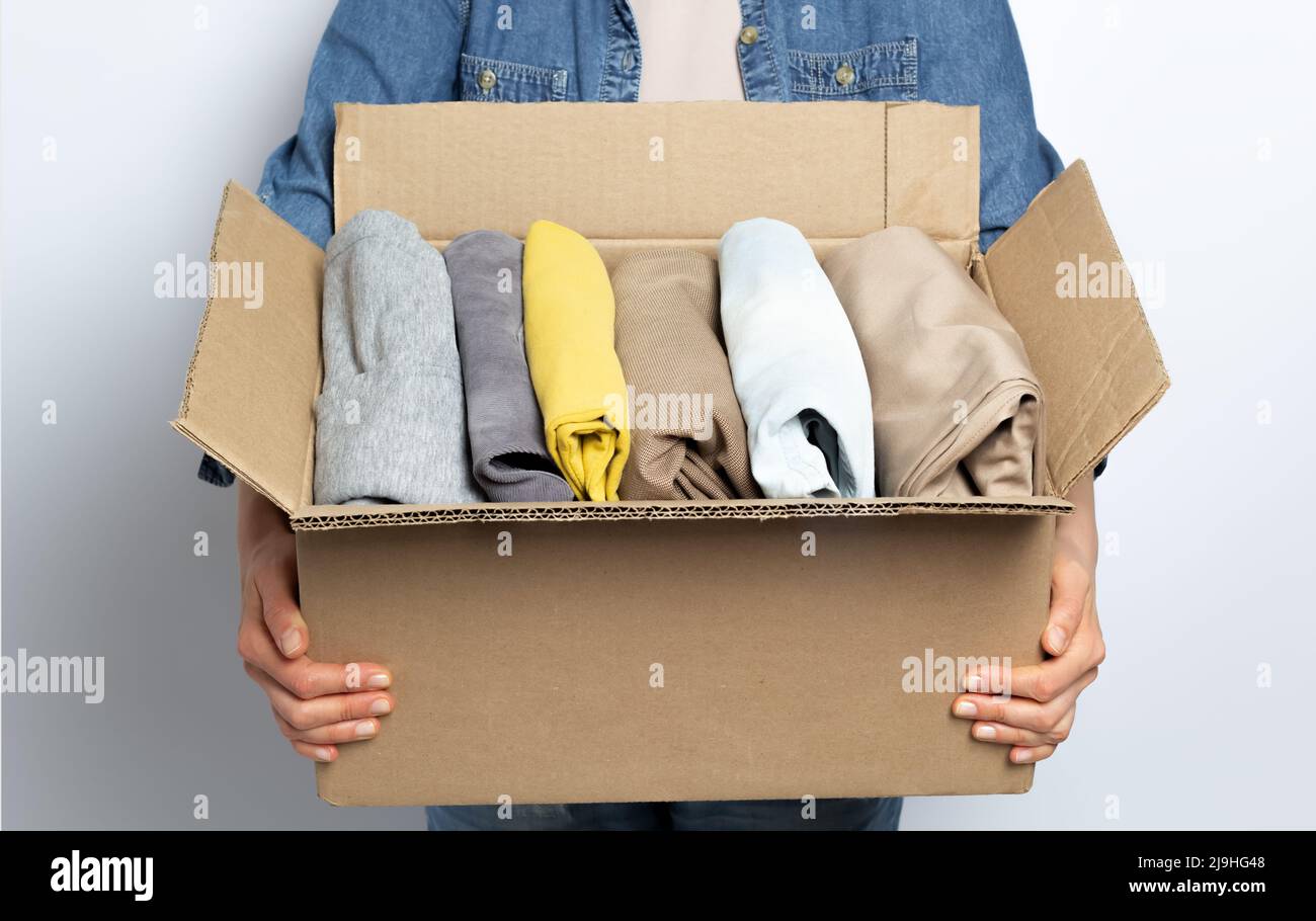 A woman is holding a box with donation or charity clothes in her hands. Stock Photo