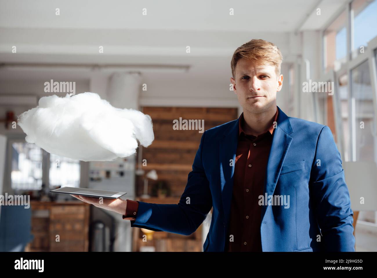 Businessman holding tablet PC under levitating cloud network in office Stock Photo
