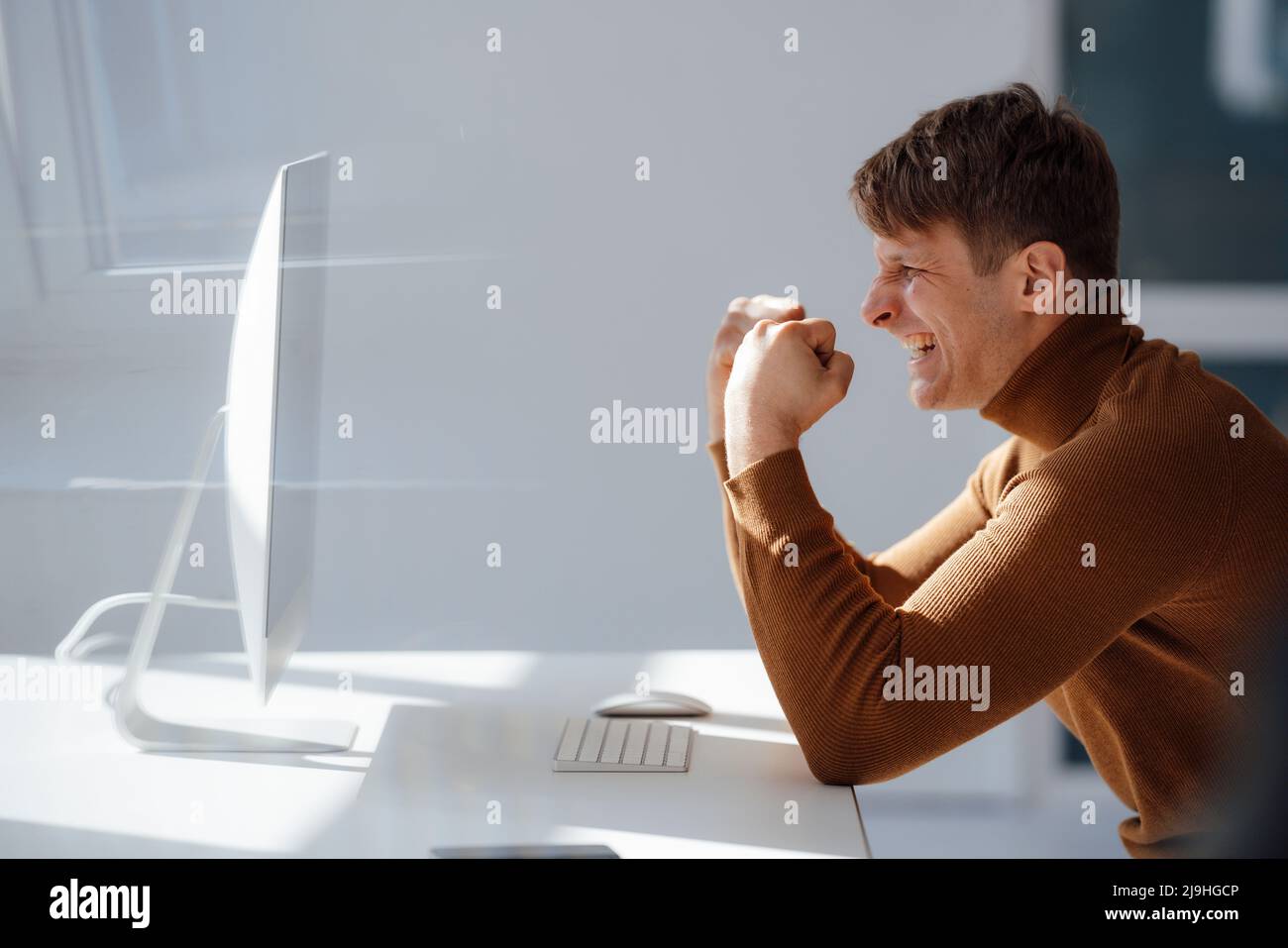 Happy businessman gesturing fist looking at desktop PC in office Stock Photo