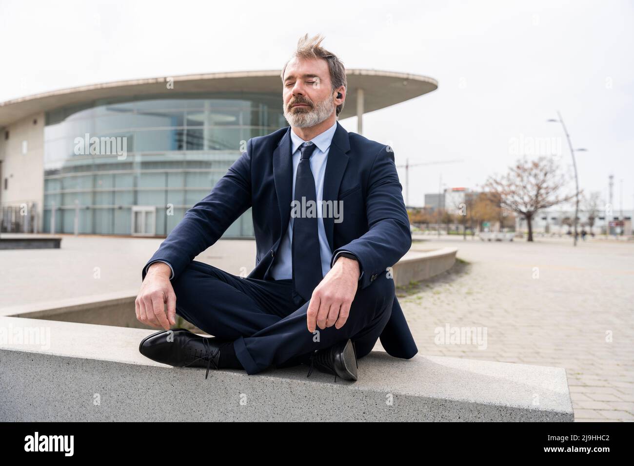 Businessman meditating sitting crossed-legged on wall Stock Photo - Alamy