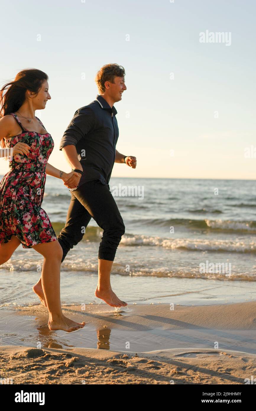 Happy couple holding hands running at beach on sunny day Stock Photo ...
