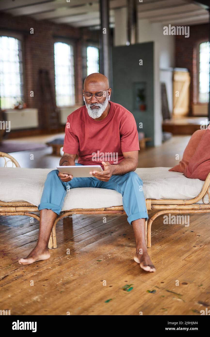 Mature man with white beard using tablet PC sitting on sofa at home Stock Photo