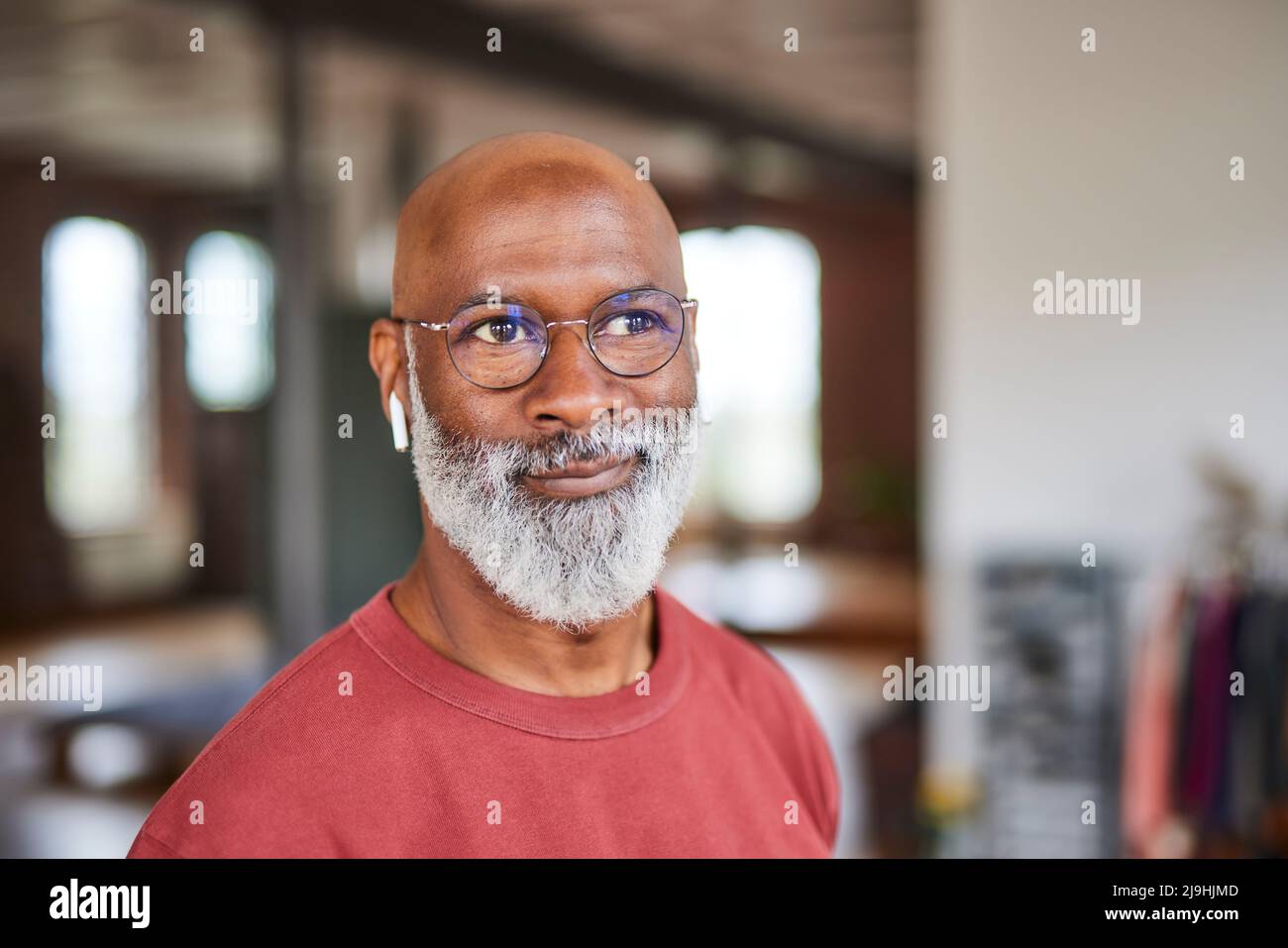 Smiling bald man with grey beard wearing eyeglasses at home Stock Photo