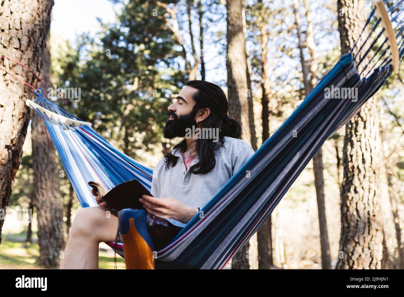 Disabled man with eyes closed holding diary sitting in hammock Stock Photo