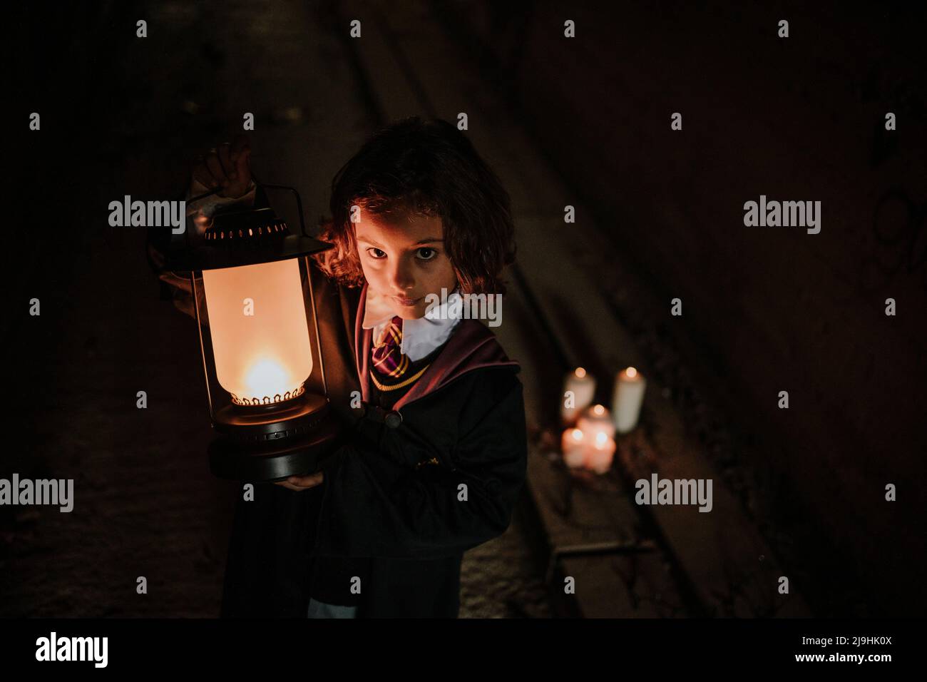 Girl with lantern wearing witch costume standing in spooky dark tunnel Stock Photo