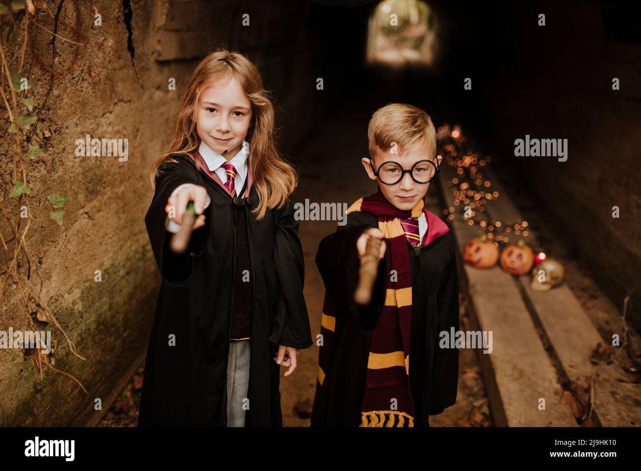 Boy and girl in witch and wizard costumes pointing magic wands Stock Photo