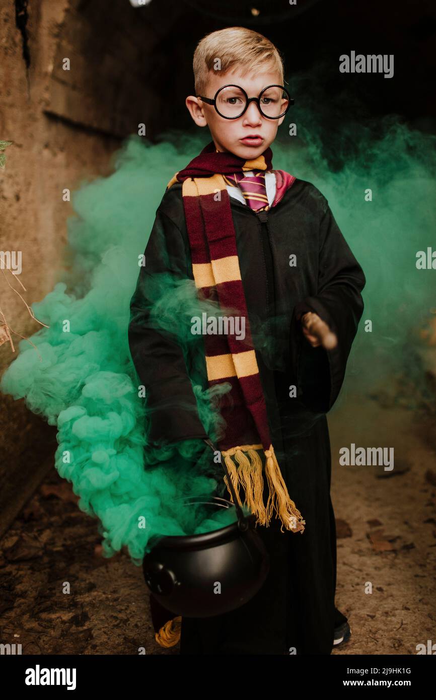 Boy holding magic cauldron with green smoke standing in tunnel at Halloween Stock Photo