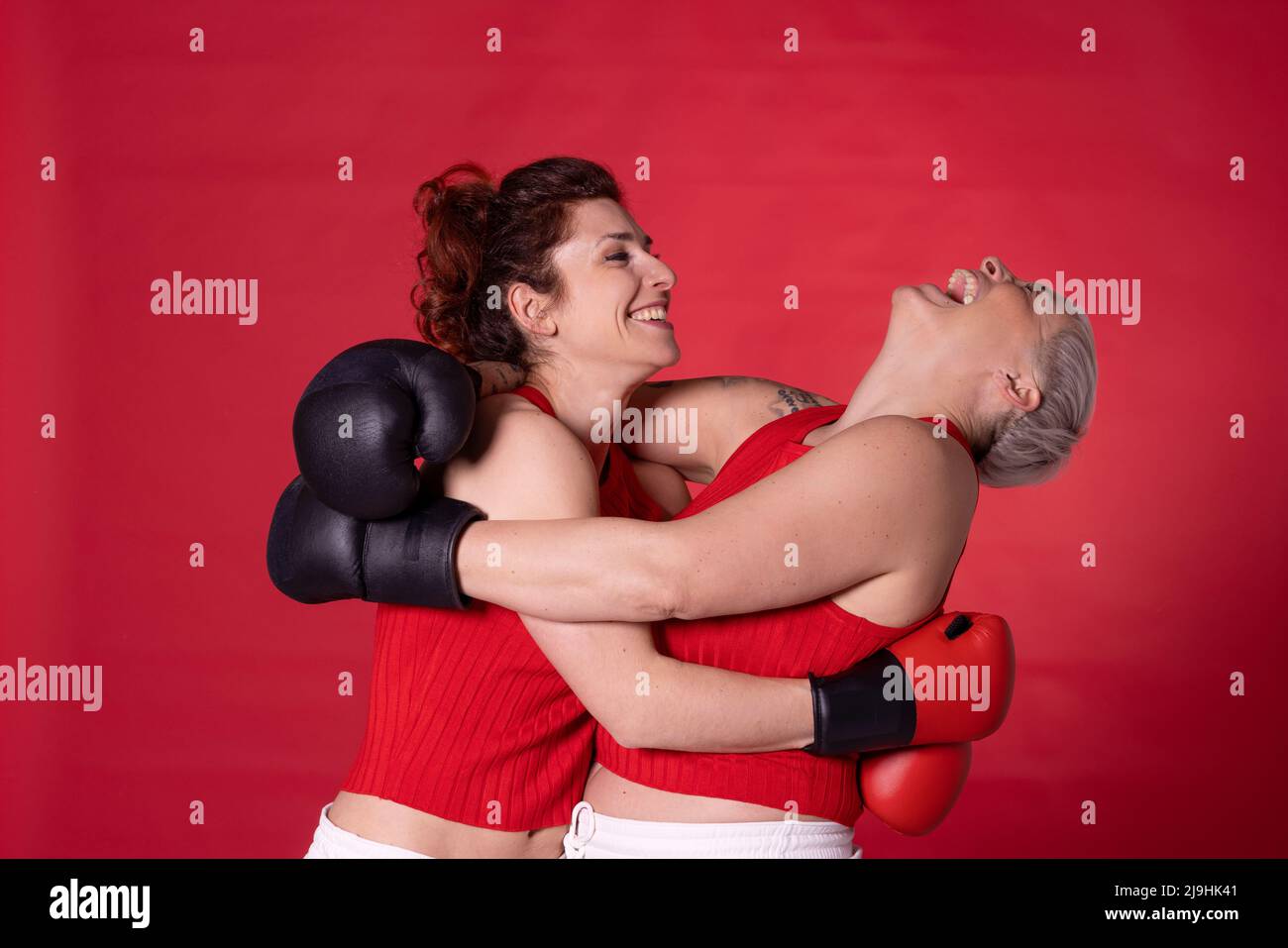 Happy friends wearing boxing gloves hugging each other against red ...