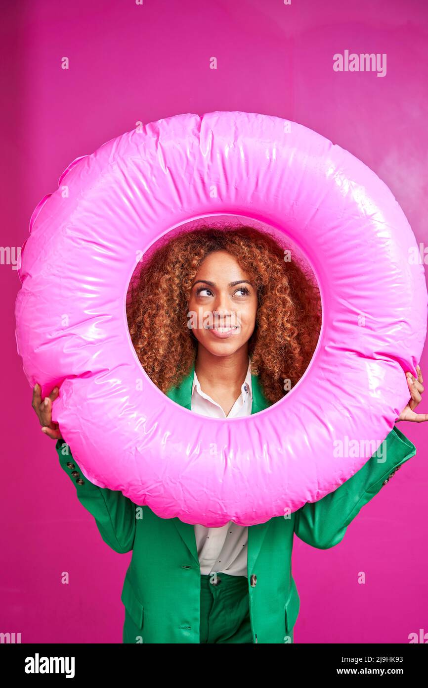 Smiling businesswoman looking though inflatable ring against pink background Stock Photo