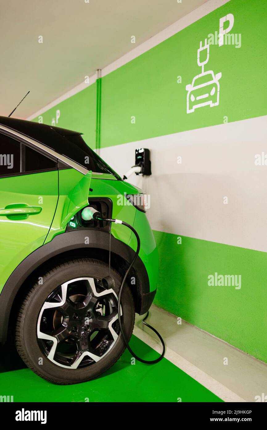 Green car being charged by wall at electric charging station Stock Photo