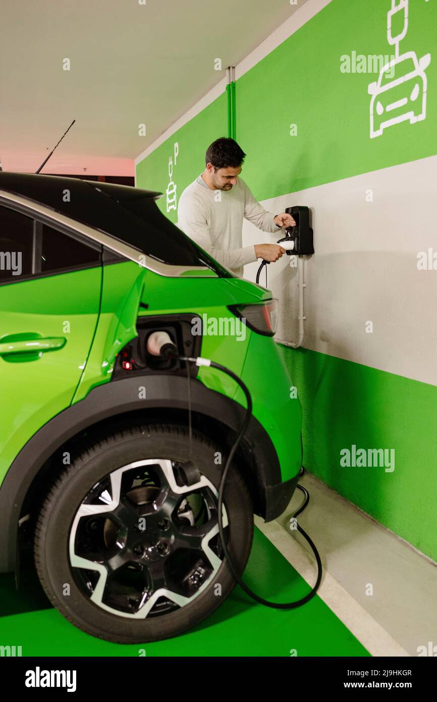 Man plugging cord to charge electric car at charging station Stock Photo