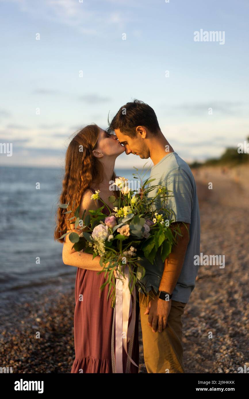 Woman holding bouquet kissing on man's forehead at beach Stock Photo