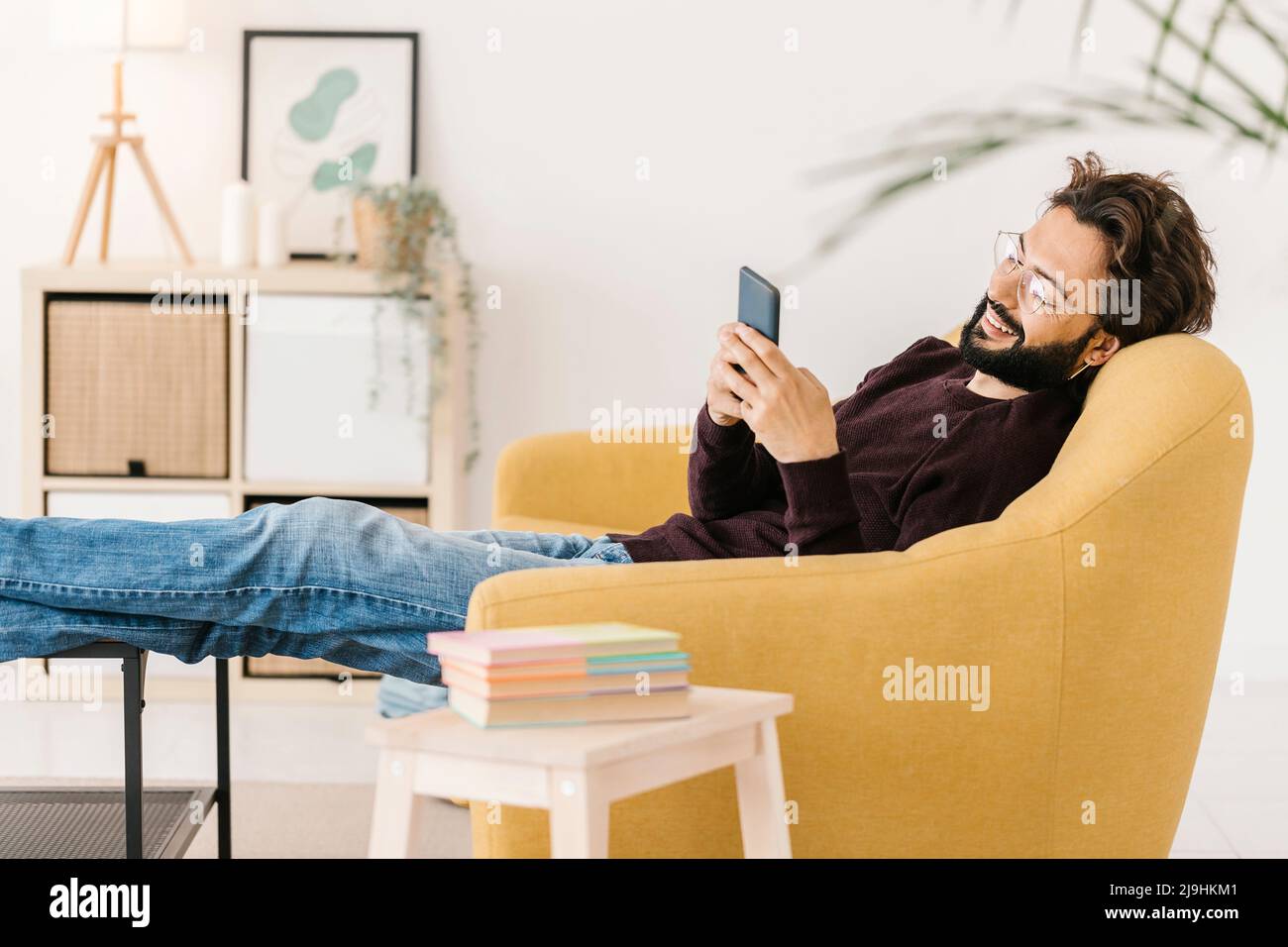 Relaxed man using smart phone sitting on sofa at home Stock Photo