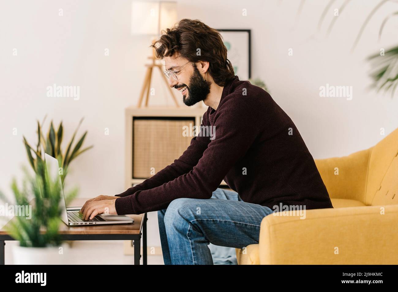 Smiling bearded man using laptop sitting on sofa at home Stock Photo