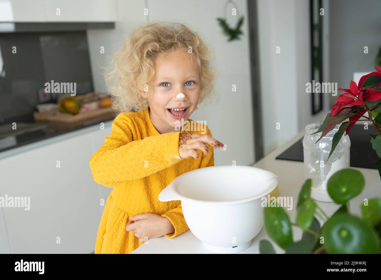 Happy blond girl with bowl standing at kitchen island Stock Photo