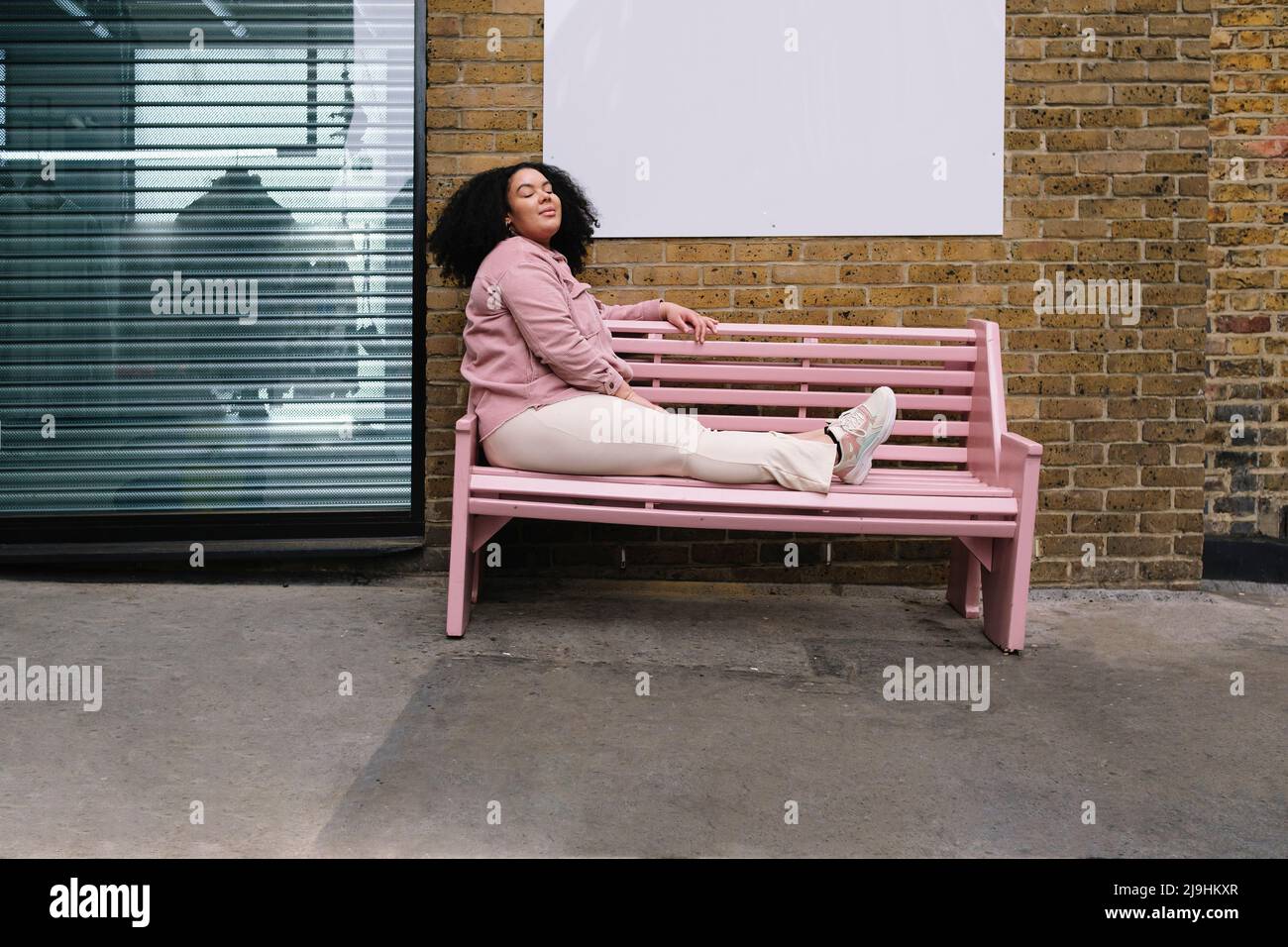 Young woman with eyes closed sitting on pink bench Stock Photo