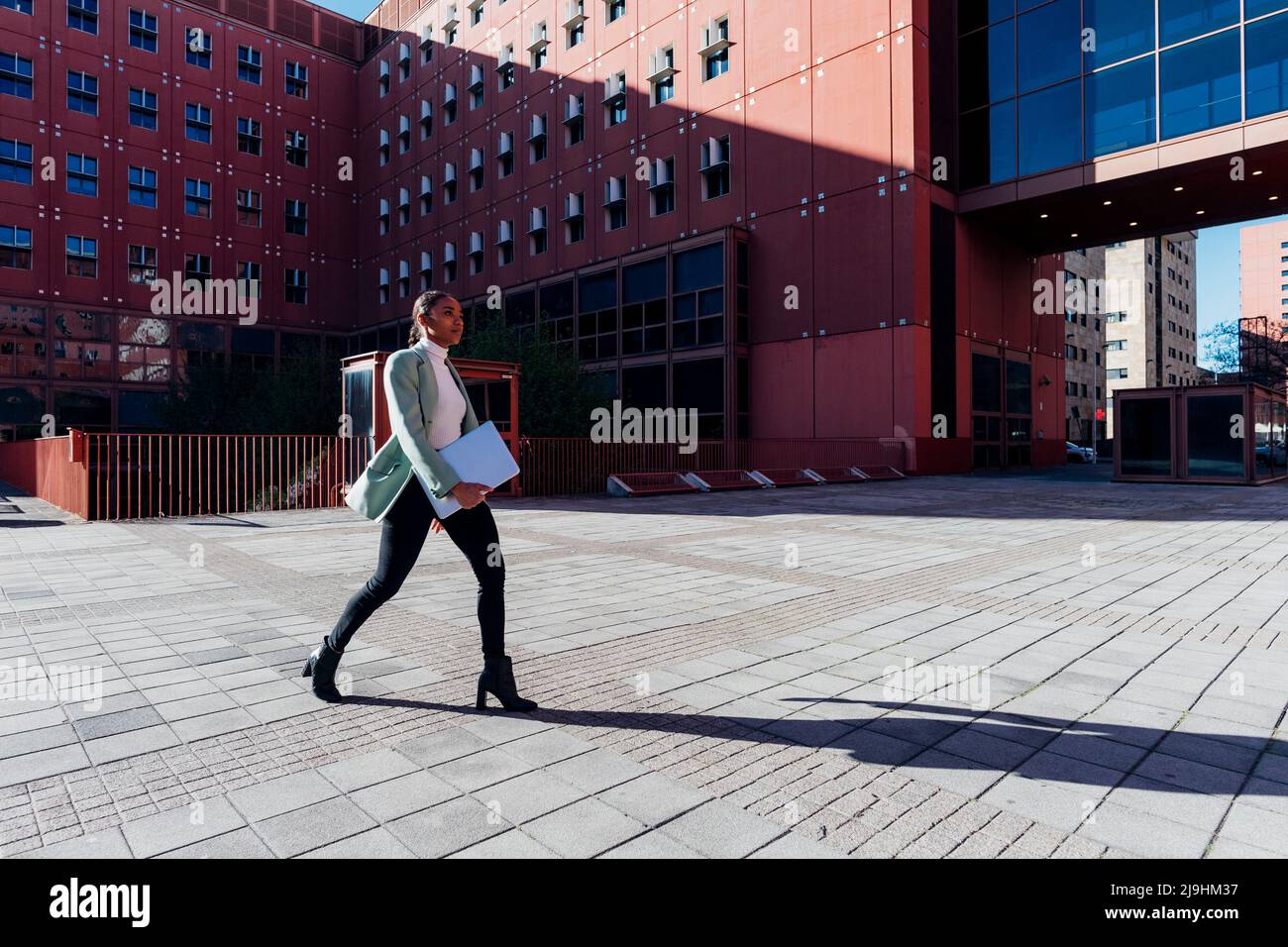 Young businesswoman with laptop walking in downtown district Stock Photo