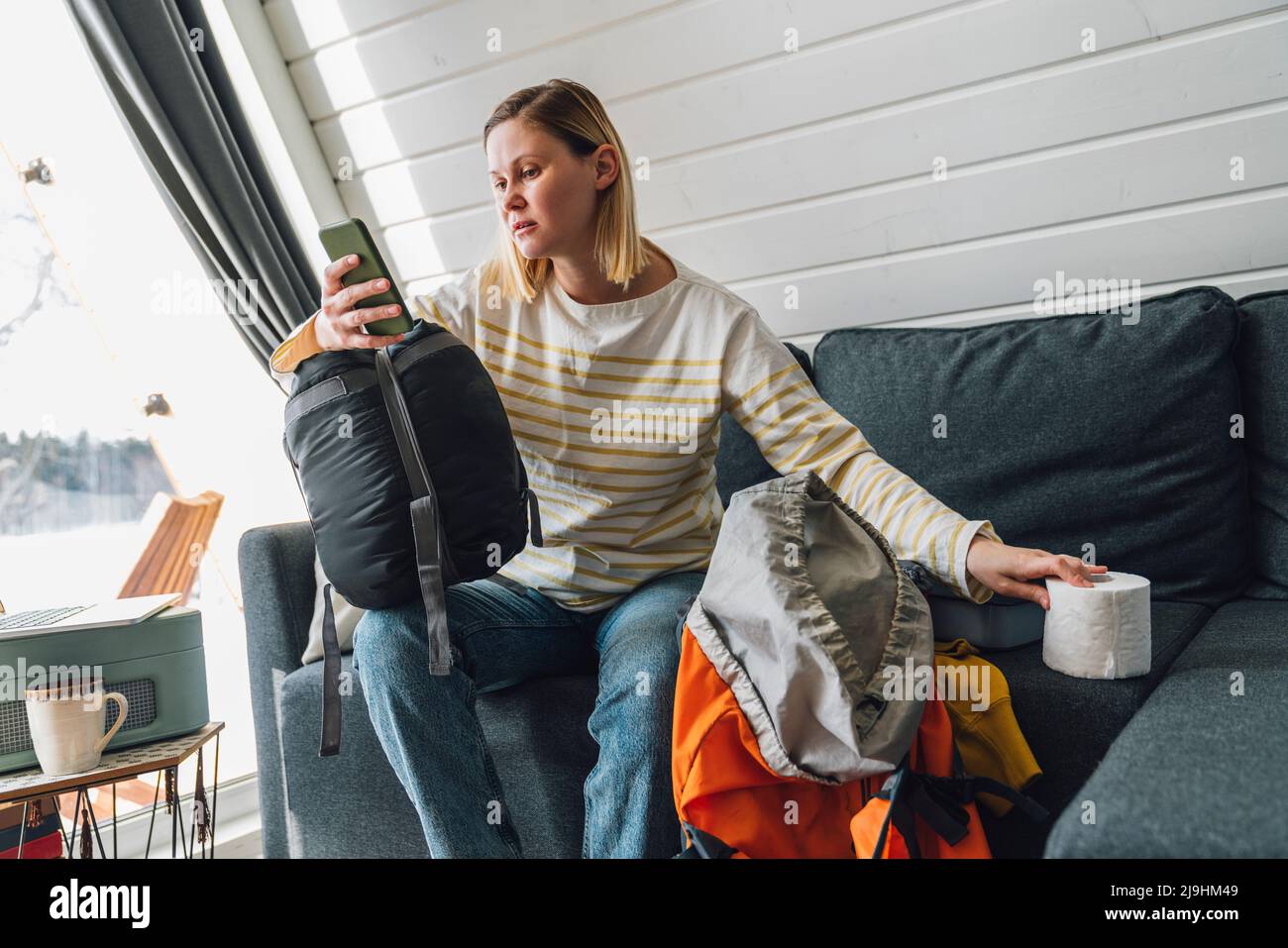 Woman using smart phone holding toilet paper sitting on sofa at home Stock Photo