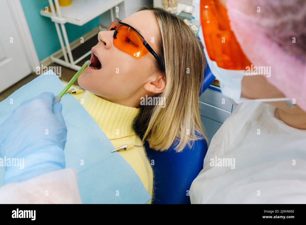 A young beautiful girl in dental glasses treats her teeth at the