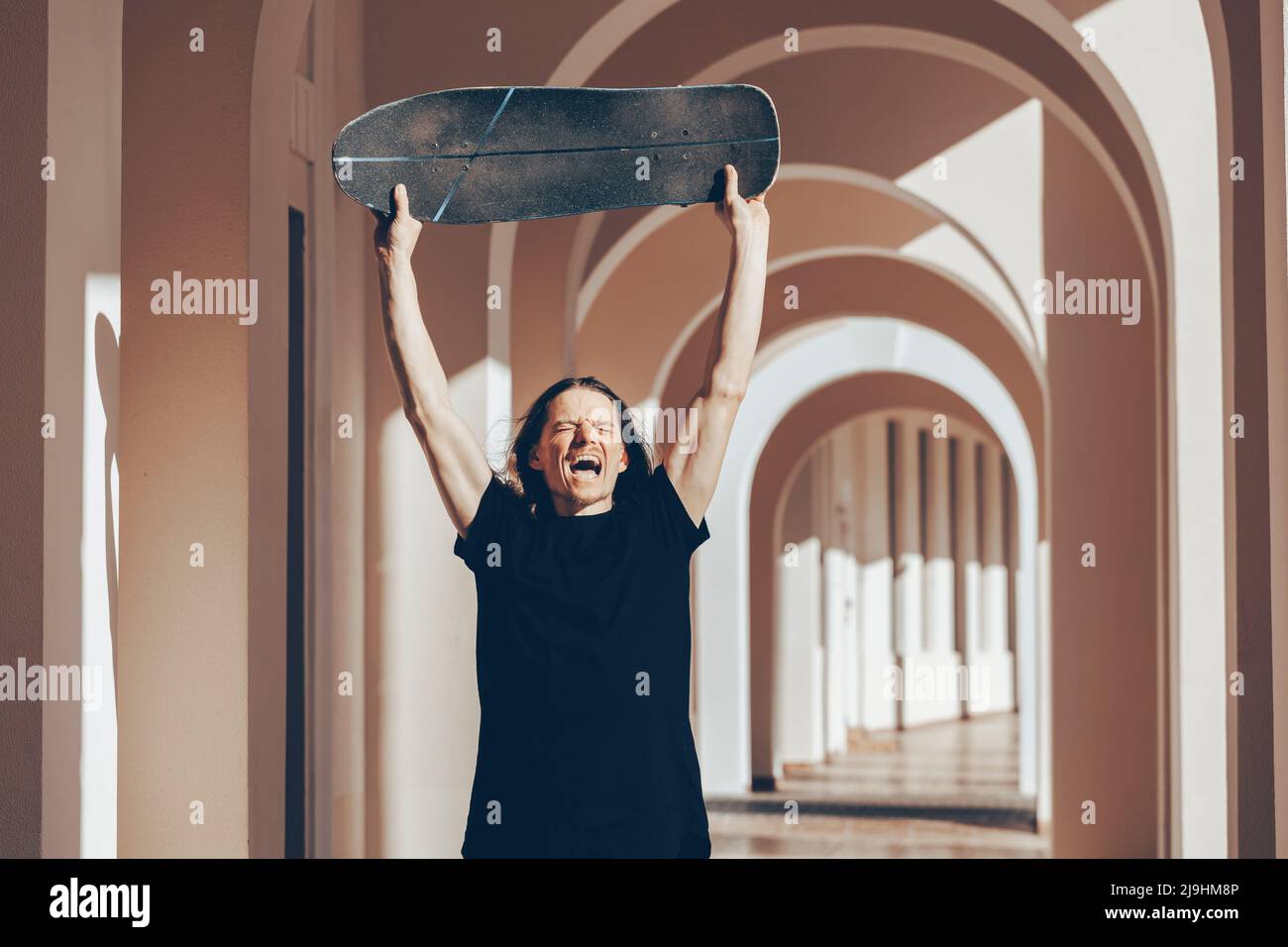 Man lifting skateboard above head shouting in arcade Stock Photo