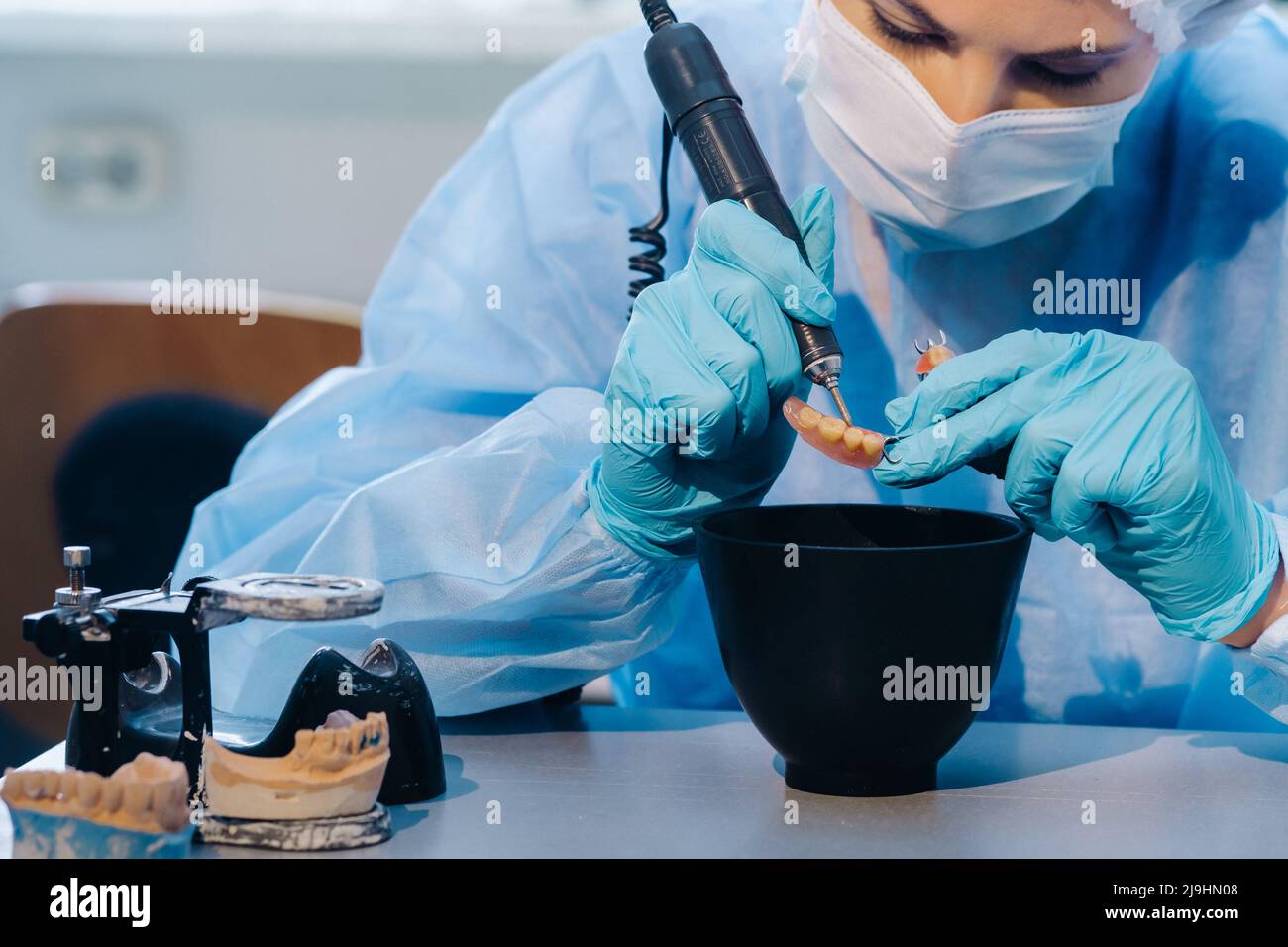 A dental technician in protective clothing is working on a prosthetic tooth in his laboratory