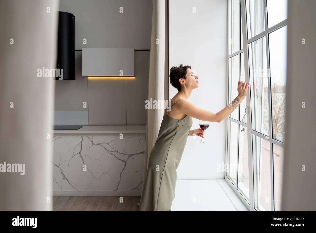 Woman holding wineglass opening window at home Stock Photo