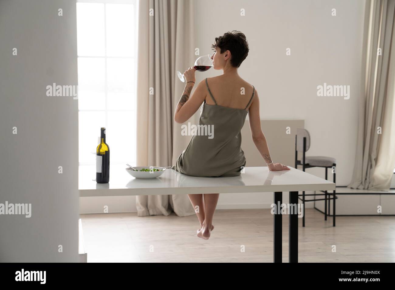 Woman drinking red wine sitting on table at home Stock Photo