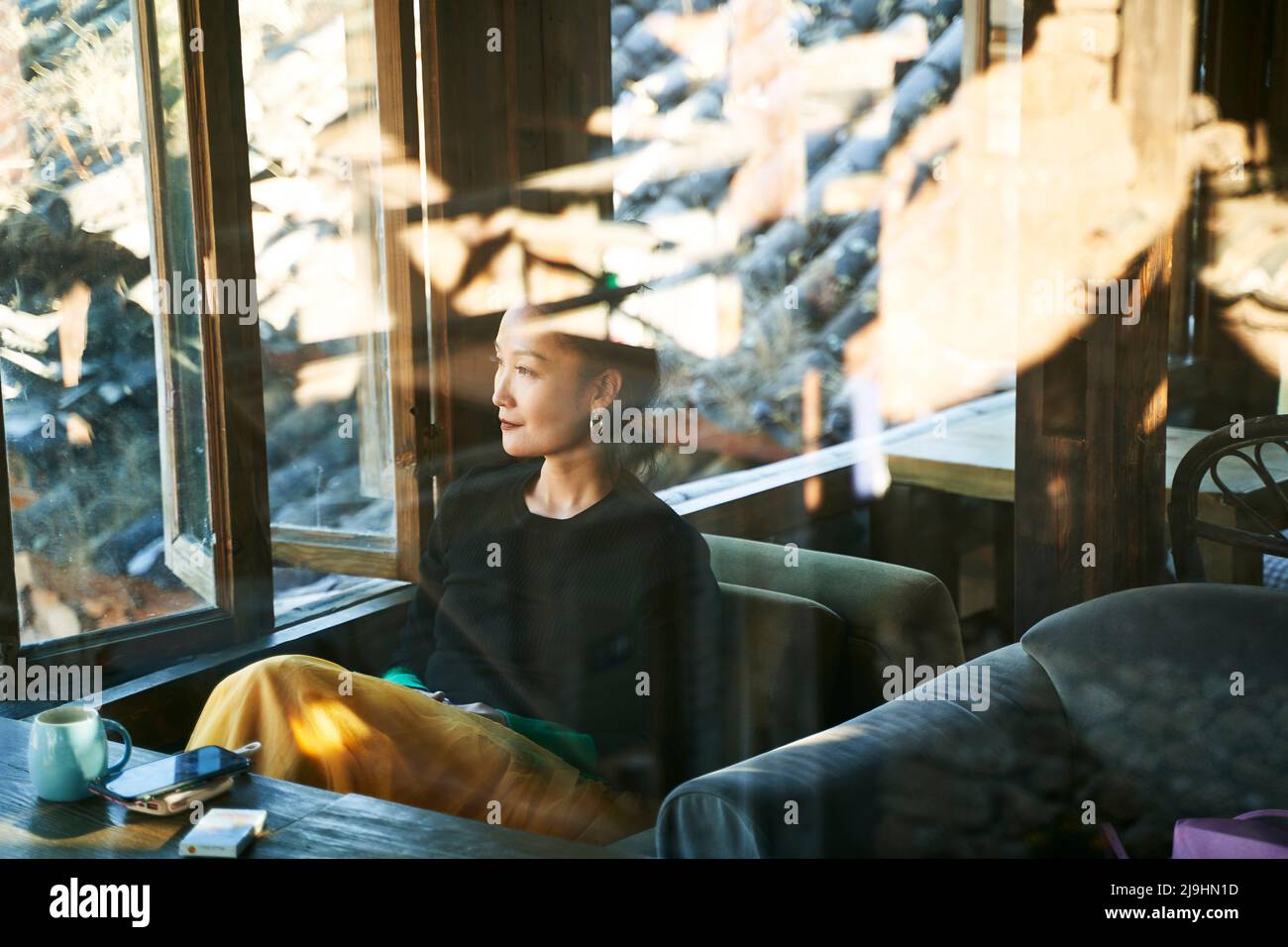 through the glass shot of an asian woman sitting in sofa relaxing in a coffee shop Stock Photo