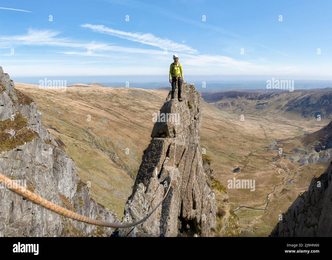 Senior woman standing on top of rocky mountain peak with climbing rope Stock Photo