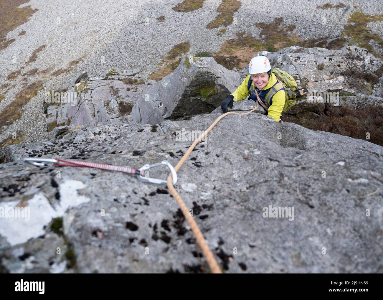 Happy active senior woman with rope climbing rocky mountain Stock Photo