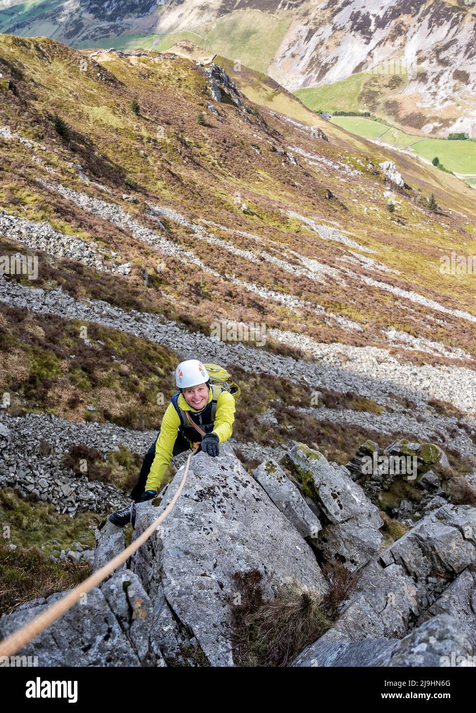 Smiling senior woman with rope climbing rocky mountain Stock Photo