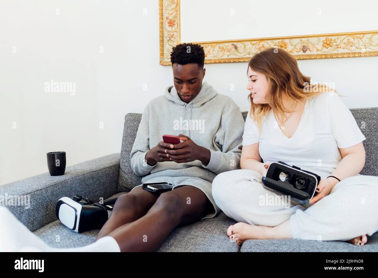 Young man using smart phone sitting by girlfriend on sofa at home Stock Photo